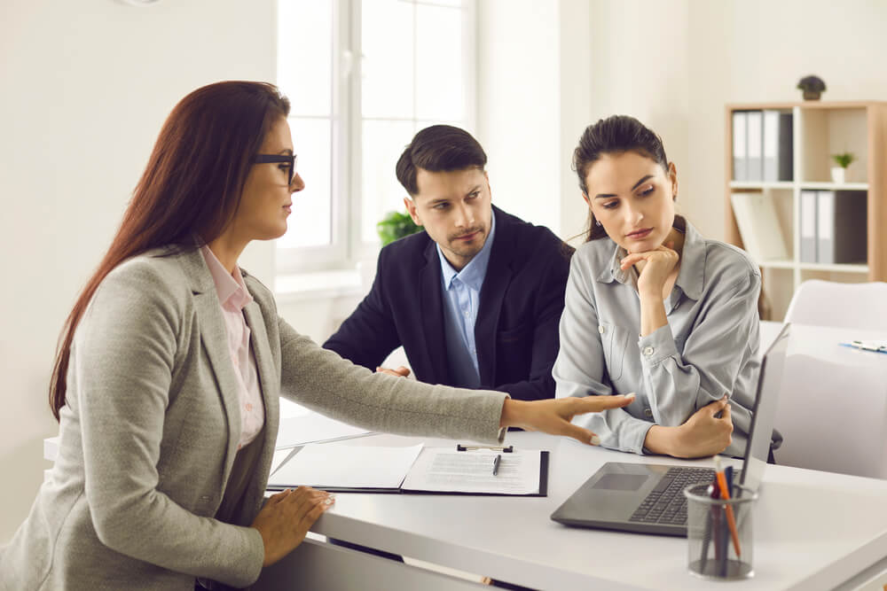 Office Meeting With Real Estate Agent. Couple of Serious Future Buyers Considering House Variants and Options on Computer Screen